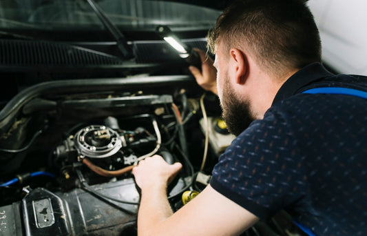 Mechanic working on a car engine with tools and equipment visible.